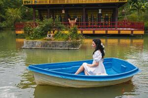A young female traveler is sailing on a wooden boat on a lake against the background of a Buddhist temple standing on the water photo