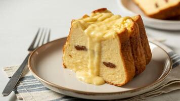 A slice of bread pudding with custard sauce on a plate next to a fork and napkin photo