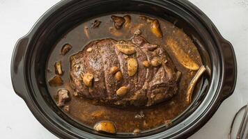 Close up of a pot roast with mushrooms and garlic in a black slow cooker pot photo