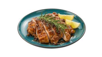 Sliced glazed chicken with rosemary and lemon wedges on a teal colored plate photo