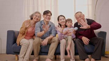 A family enjoys quality time together, waving at the camera with warmth and happiness. Different generations share laughter in a bright living room filled with love. video