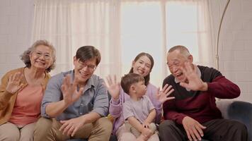 A family enjoys quality time together, waving at the camera with warmth and happiness. Different generations share laughter in a bright living room with love. video