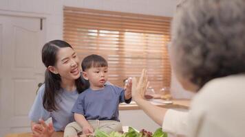 Mother and young child share a joyful moment during lunch at their kitchen table. They engage with a family member, creating a vibrant and warm atmosphere. video