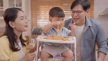 In a cozy kitchen, a cheerful family engages in playful dining while their young child explores spaghetti. Laughter fills the air as they share a lighthearted moment together. video