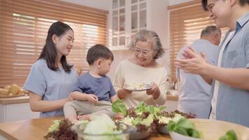 A joyful family gathers in the kitchen, preparing a fresh salad. Laughter fills the air as a child sits in his grandmother's lap, surrounded by loved ones. Fresh ingredients are being prepped. video