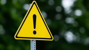 Closeup of a Triangular Yellow Warning Sign with Exclamation Mark Against a Green Foliage Background video