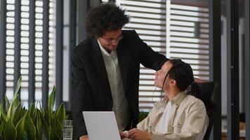 Business intern worker man working with laptop in office African American leader boss mentor coming help talking together two diversity businessmen colleagues discuss internet web data difficulty photo