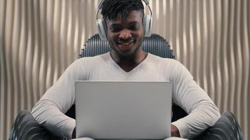 Futurism African American man male programmer developer smiling cyber data guy in white futuristic room indoors cyberspace modern technology wearing wireless headphones typing laptop work online app photo