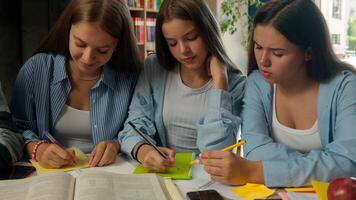 Four teenagers classmates together preparing for exams writing notes happy concentrated write homework task study education studying pupils students in school library table teamwork focused learning photo