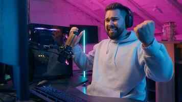 Smiling Caucasian man guy male gamer streamer playing online game at night lost upset frustrated angry mad furious with bad result failure addiction streaming in neon room player bangs fists on table photo