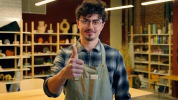 A man in an apron is giving a thumbs up in a pottery studio setting photo