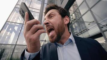 Mad middle-aged Caucasian business man shouting scolding yelling angry to mobile phone conversation arguing problem argument quarrel near office building in city businessman male work failure fury job photo