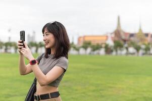 Happy southeast asian woman teenager blogger on solo world travel take photo with smartphone for local cultural experience. cheerful explorer enjoying asia tourism concept in Bangkok Thailand