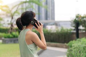 Asian woman in 30s gets fitness workout advice from trainer on smartphone. An exercise for healthy lifestyle and wellness with technology in an urban city at sunset for healthcare photo