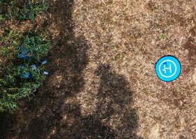 Drone landing pad surrounded by dried grass and scattered objects in a remote area as two persons sit underneath the shade photo