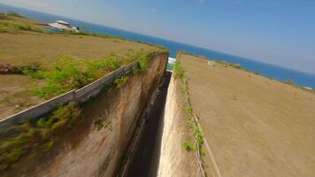 Immersive FPV drone flight along coastal road carved between limestone cliffs and turquoise sea at Batu Barak Beach, Bali, Indonesia. video