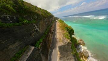 Cinematic FPV drone flight along Pandawa Beach in Bali, showcasing turquoise sea, golden sand, and coastal road carved into limestone cliffs. video