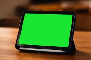 A side view of a tablet device with a blank green screen on the table photo