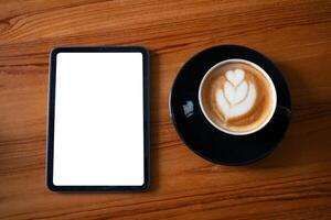 Tablet with blank white screen display beside a black cup of cappuccino on natural wood. photo