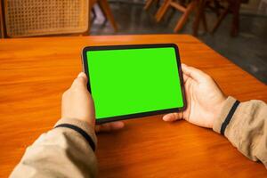 Man viewing a tablet with a blank green screen in a cozy cafe setting photo