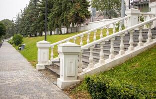 Vintage white stone staircase with balustrade against a grass-covered slope in a summer park, side view photo