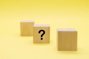 One light wooden block with a black question mark on yellow background photo