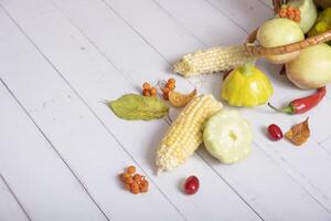Fragment of autumn harvest basket with corn, apples, zucchini and peppers on wooden background decorated autumn leaves photo