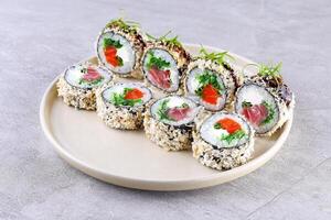 Tempura roll with tuna and spicy sauce on black slate on stone background. Hot sushi roll with chopsticks in contemporary composition. Maki sushi with tuna shavings in minimal style photo