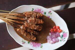 chicken satay with peanut sauce, sliced onions, sliced red chili in white plate. sate ayam. Indonesian food. photo