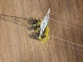 Power lines intersect with a field surrounded by autumn foliage in a rural landscape during midday photo