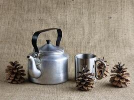 Aluminum army teapot from the Second World War. Stylized still life with a cup and pine cones. Soviet soldier's teapot. Close-up. Burlap background. photo