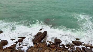 A vivid coastal scene featuring waves dramatically crashing over rugged rocks amidst calming tranquil waters photo