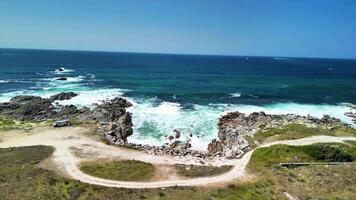 Experience stunning coastal views with roaring waves, rocky formations, and lush greenery under a clear blue sky photo