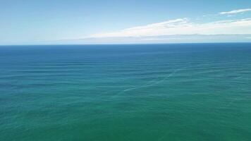 A breathtaking aerial view showcases the calm, serene ocean waters with gentle waves beneath a clear, bright blue sky photo