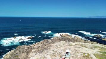 A breathtaking view of the vast ocean with crashing waves, a rugged rocky coastline, and clear blue skies above photo