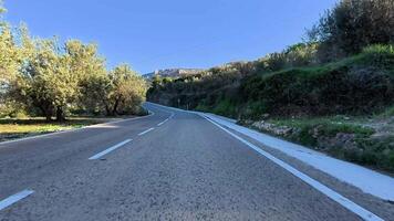 A picturesque view of a winding road surrounded by olive trees and rocky hills under clear blue skies. photo