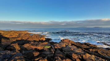 A beautifully tranquil seaside view featuring rugged, majestic rocks and gentle waves under a clear blue sky photo