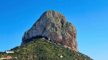 A breathtaking view of an enormous rock formation gracefully surrounded by lush, vibrant greenery and clear blue skies photo