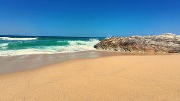 A picturesque beach scene featuring soft sand, gentle waves, and a large rock formation under a clear sky. photo