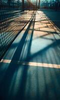Sunlight filtering through netting creates dramatic shadows across a tennis court surface outdoors casting light patterns photo