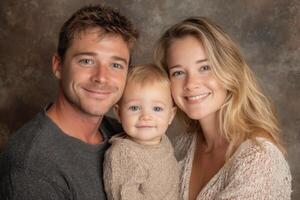 Parents joyfully pose with their adorable baby, all wearing soft, neutral clothing, in a warm, inviting studio atmosphere photo