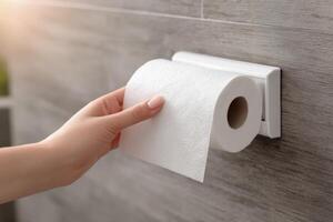 A hand is gripping a roll of toilet paper on a holder mounted on a wall in a sleek, modern bathroom photo