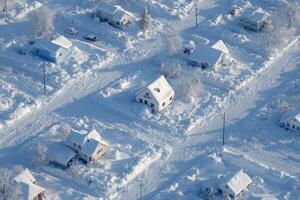 Aerial view of a suburban neighborhood blanketed in snow, showcasing houses surrounded by deep snow drifts beneath a bright sky photo