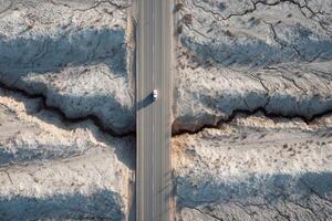 A lone vehicle navigates a cracked and arid landscape under clear skies, highlighting drought's impact on the terrain photo