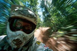 A motocross biker navigates a dirt trail amidst trees, creating a cloud of dust during a thrilling ride in nature photo
