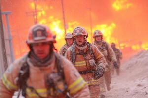 Firefighters work diligently in snow and ice as they face a fierce fire in the background, showcasing bravery amid dangerous conditions photo