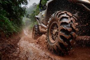 A rugged vehicle maneuvers through a muddy trail surrounded by lush greenery on a cloudy afternoon, splashing dirt and water photo