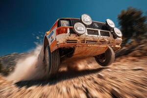 A rally car speeds across rocky ground, kicking up dust under a clear blue sky in a desert landscape photo