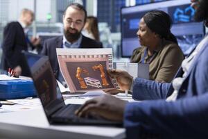 Industrial plant managers look over schematics, planning facility upgrades using laptop. Factory shareholders look over conveyor belts blueprints, working on notebook device photo