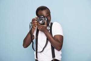 African American man holding a DSLR camera up to his face, preparing to take a professional shot. Black male model standing in a studio, focused and poised, showcasing his photography expertise. photo